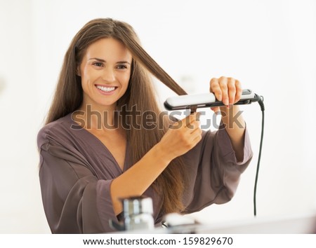 Happy young woman straightening hair with straightener