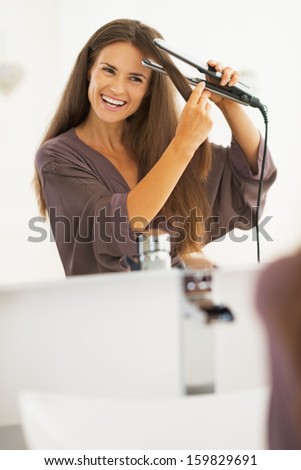 Smiling young woman straightening hair with straightener