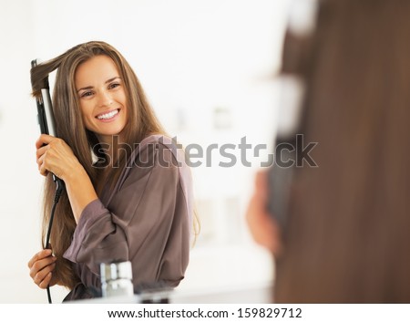Smiling Woman Curling Hair With Straightener