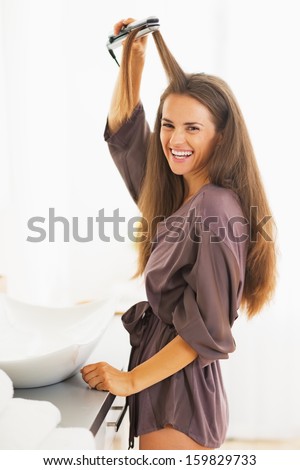 Portrait of smiling young woman straightening hair with straightener
