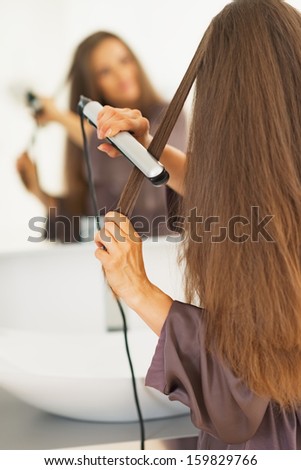 Woman straightening hair with straightener . rear view