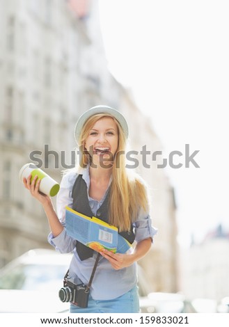 Happy tourist girl with map and cup of hot beverage on city street