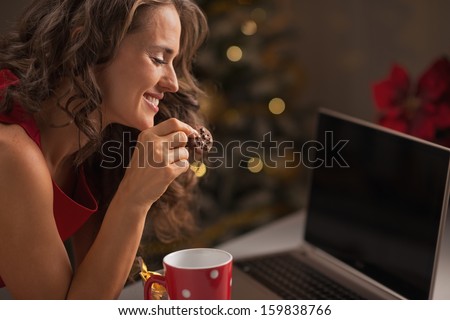 Happy woman having christmas cookies with cup of hot chocolate and usign laptop