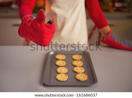 Closeup on young housewife in kitchen gloves showing thumbs up and christmas cookies on pan