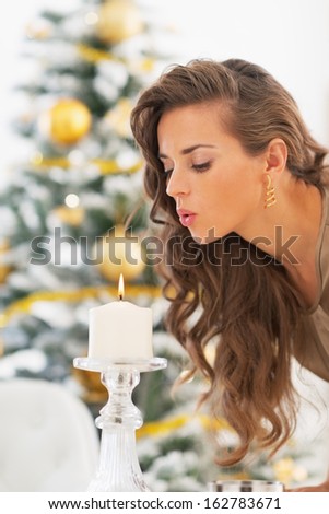 Young woman blowing out candle in front of christmas tree