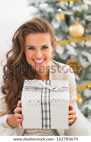 Smiling young woman holding christmas present box in front of christmas tree