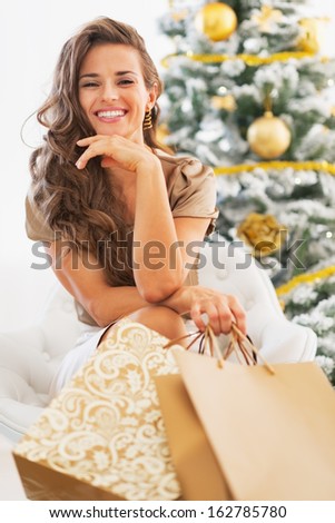 Portrait of happy young woman with shopping bags sitting near christmas tree