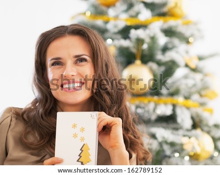 Portrait of happy young woman and christmas postcard near christmas tree