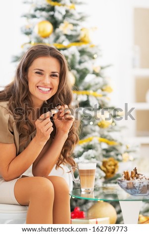Happy young woman having latte macchiato and chocolate candies near christmas tree
