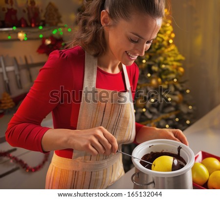 Happy young housewife making apple in chocolate glaze in christmas decorated kitchen