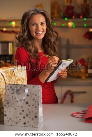 Happy young woman with shopping bags checking list of gifts in christmas decorated kitchen
