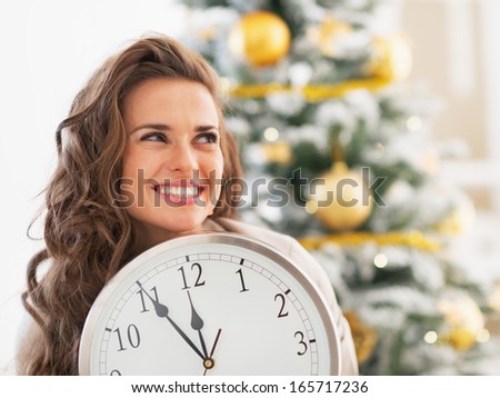 Portrait of young woman with clock looking on copy space in front of christmas tree