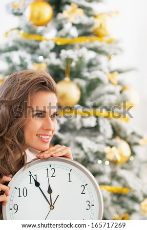 Portrait of happy young woman with clock in front of christmas tree
