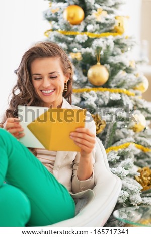 Happy young woman opening christmas letter in front of christmas tree