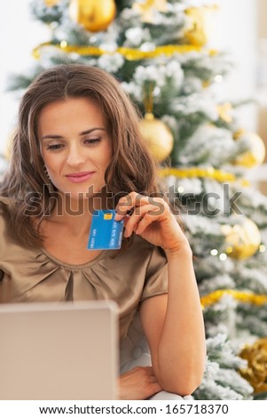 Portrait of happy young woman with credit card and laptop near christmas tree
