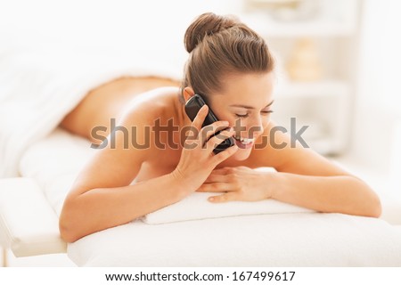 Happy young woman talking mobile phone while laying on massage table