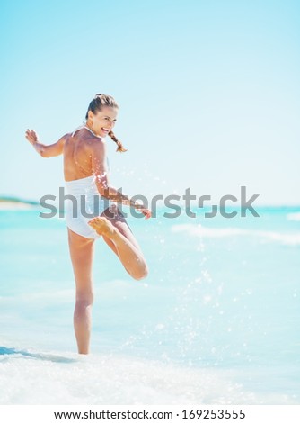 Full length portrait of smiling young woman playing with waves on beach