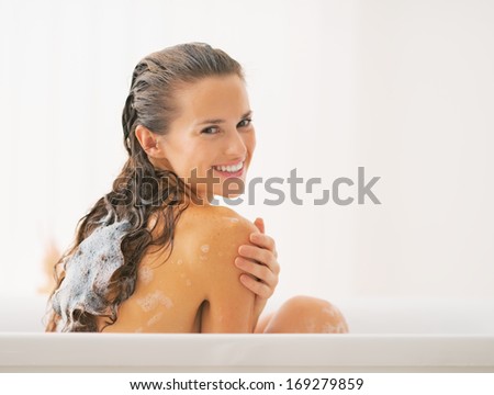 Smiling young woman washing hair in bathtub