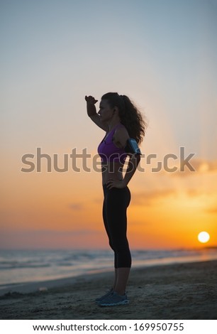 Silhouette of fitness young woman looking into distance on beach at dusk