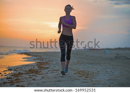 Healthy young woman running on beach in the evening