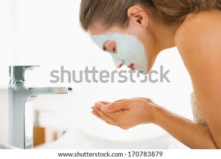 Young woman with cosmetic mask on face washing