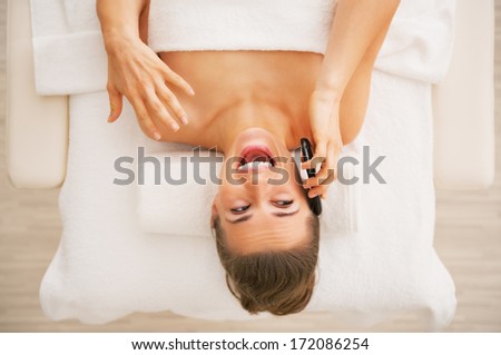 Happy young woman laying on massage table and talking cell phone