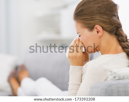 Young woman laying on sofa and blowing nose
