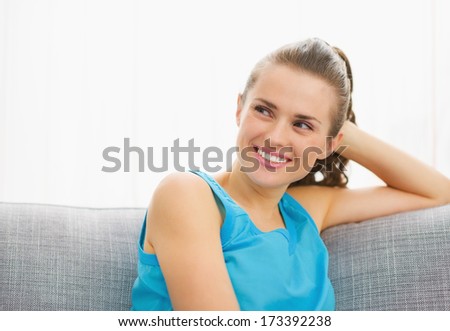 Happy young woman looking on copy space while sitting on couch