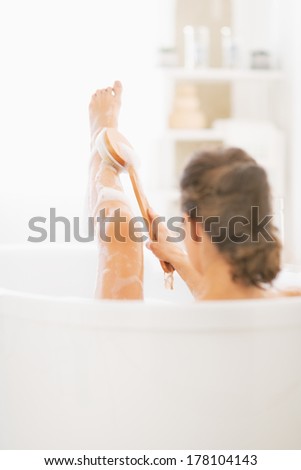 Young woman in bathtub using body brush on leg