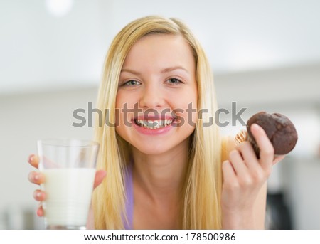 Portrait of happy young woman with milk and chocolate muffin in kitchen