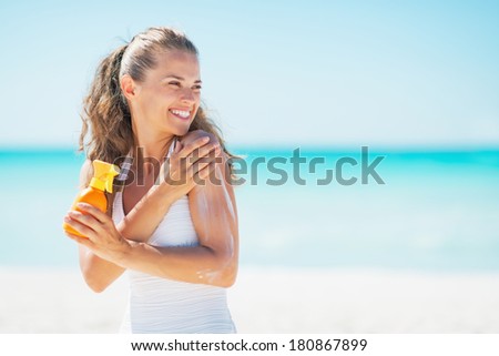 Young woman on beach applying sun block creme and looking on copy space
