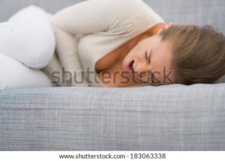 Young woman with stomach ache laying on sofa