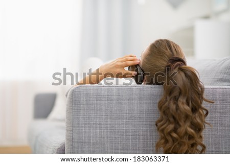 Young woman laying on sofa and talking mobile phone. rear view