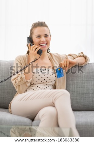 Happy young woman with credit card talking phone