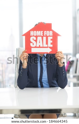 Realtor woman holding home for sale sign in front of face