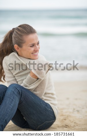 Happy young woman sitting on cold beach and looking into distance