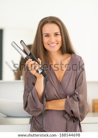 Portrait of happy young woman with hair straightener in bathroom
