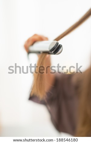 Closeup on young woman using hair straightener