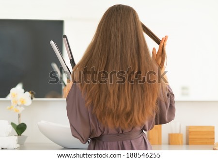 Young woman straightening hair in bathroom. rear view