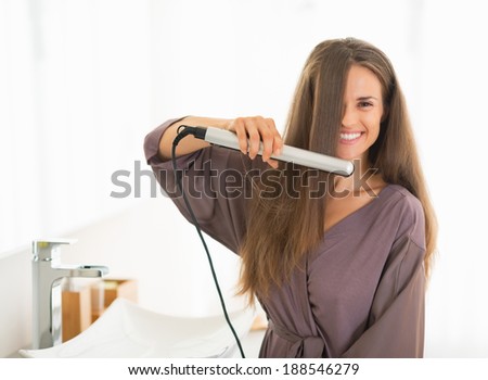 Happy young woman straightening hair in bathroom