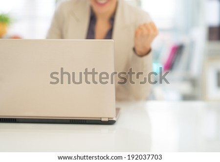 Closeup on laptop and business woman making fist pump in background