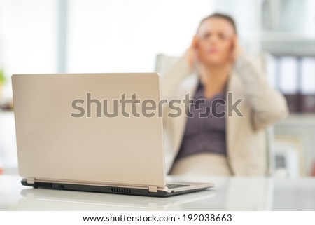 Closeup on laptop on table and stressed business woman in background