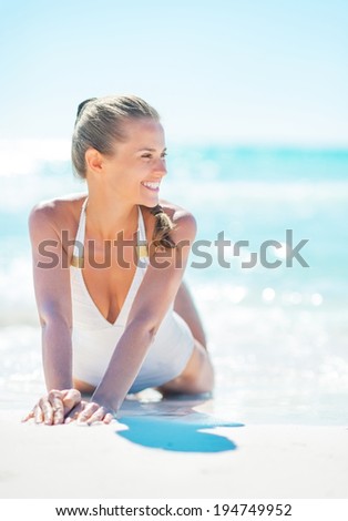 Smiling young woman sitting at seaside and looking into distance