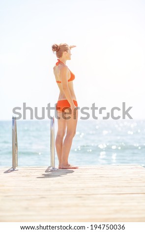Full length portrait of young woman standing on bridge and looking into distance