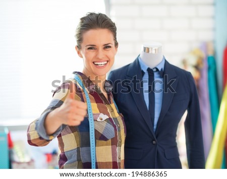 Happy seamstress near mannequin in suit showing thumbs up