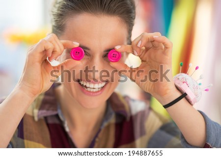 Happy seamstress holding buttons in front of eyes