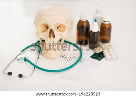Closeup on human skull stethoscope and drugs on table