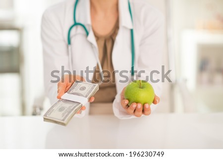 Closeup on medical doctor woman holding apple and money pack in hands