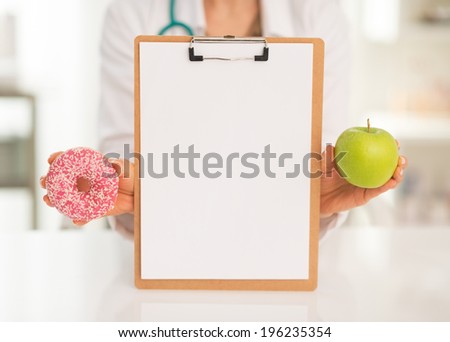 Closeup on medical doctor woman showing blank clipboard apple and donut