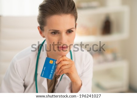 Portrait of thoughtful medical doctor woman with credit card